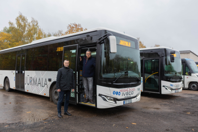 Divi vīrieši stāv pie jauna IVECO autobusa ar uzrakstu "Jūrmala"
