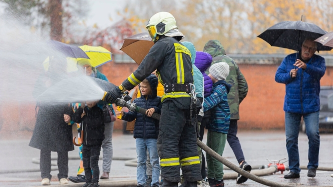 Ugunsdzēsējs māca bērniem darboties ar ūdens šļūteni