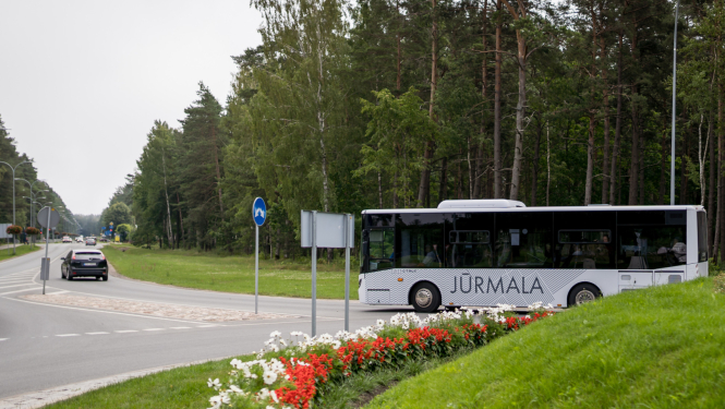 Balts sabiedriskais autobuss ar uzrakstu 'Jūrmala' brauc pa ceļu meža malā