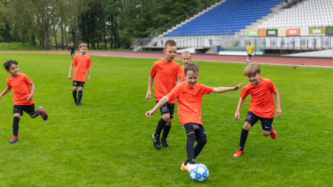 Bērni āra laukumā zaļā zālē spēlē futbolu