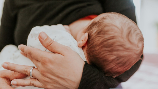 mamma zīda bērnu, turot rokās
