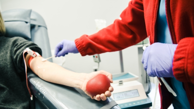 Medicīnas darbinieks ņem asins paraugu no donora, kurš rokā tur sarkanu bumbiņu.