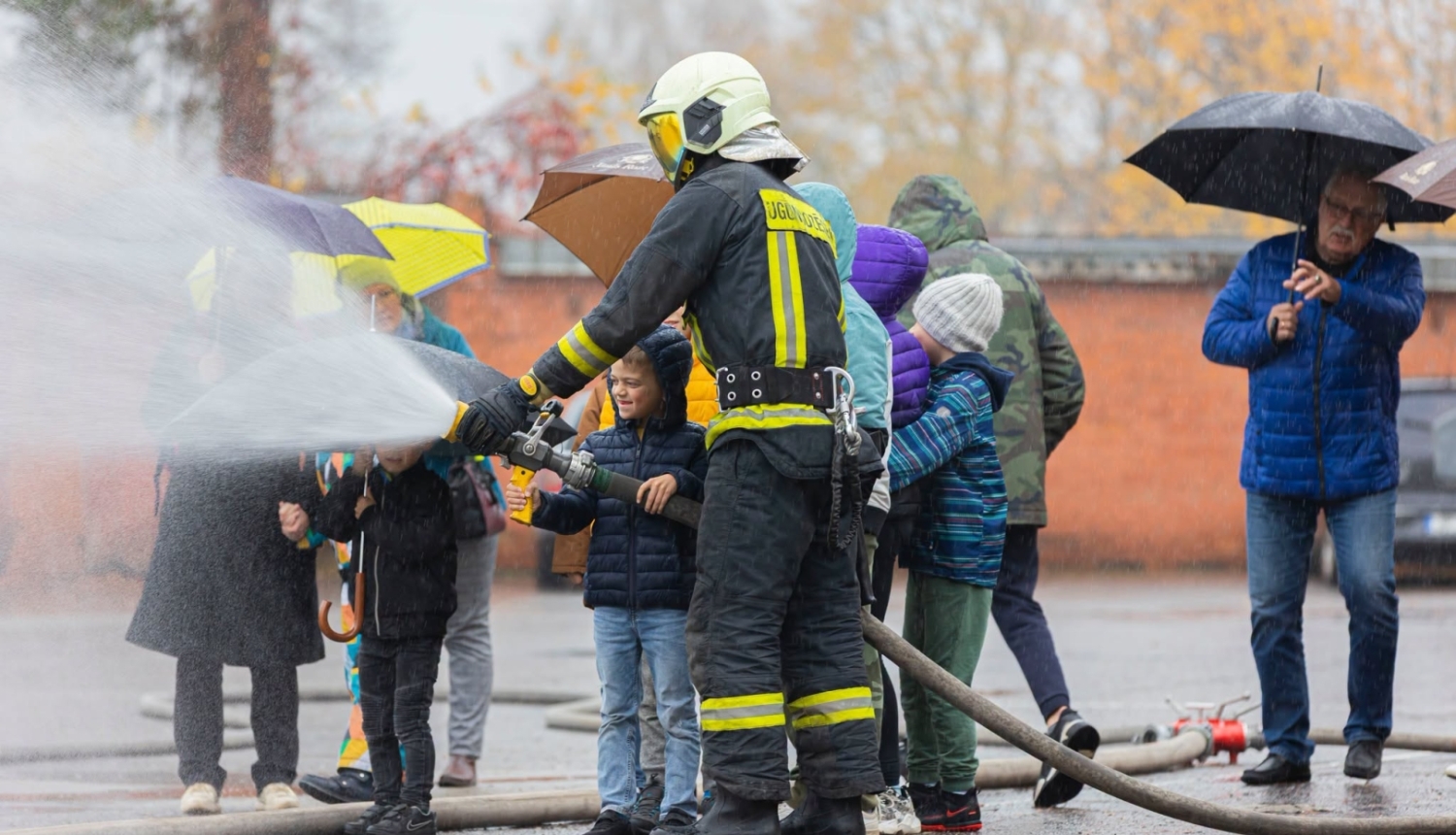 Ugunsdzēsējs māca bērniem darboties ar ūdens šļūteni