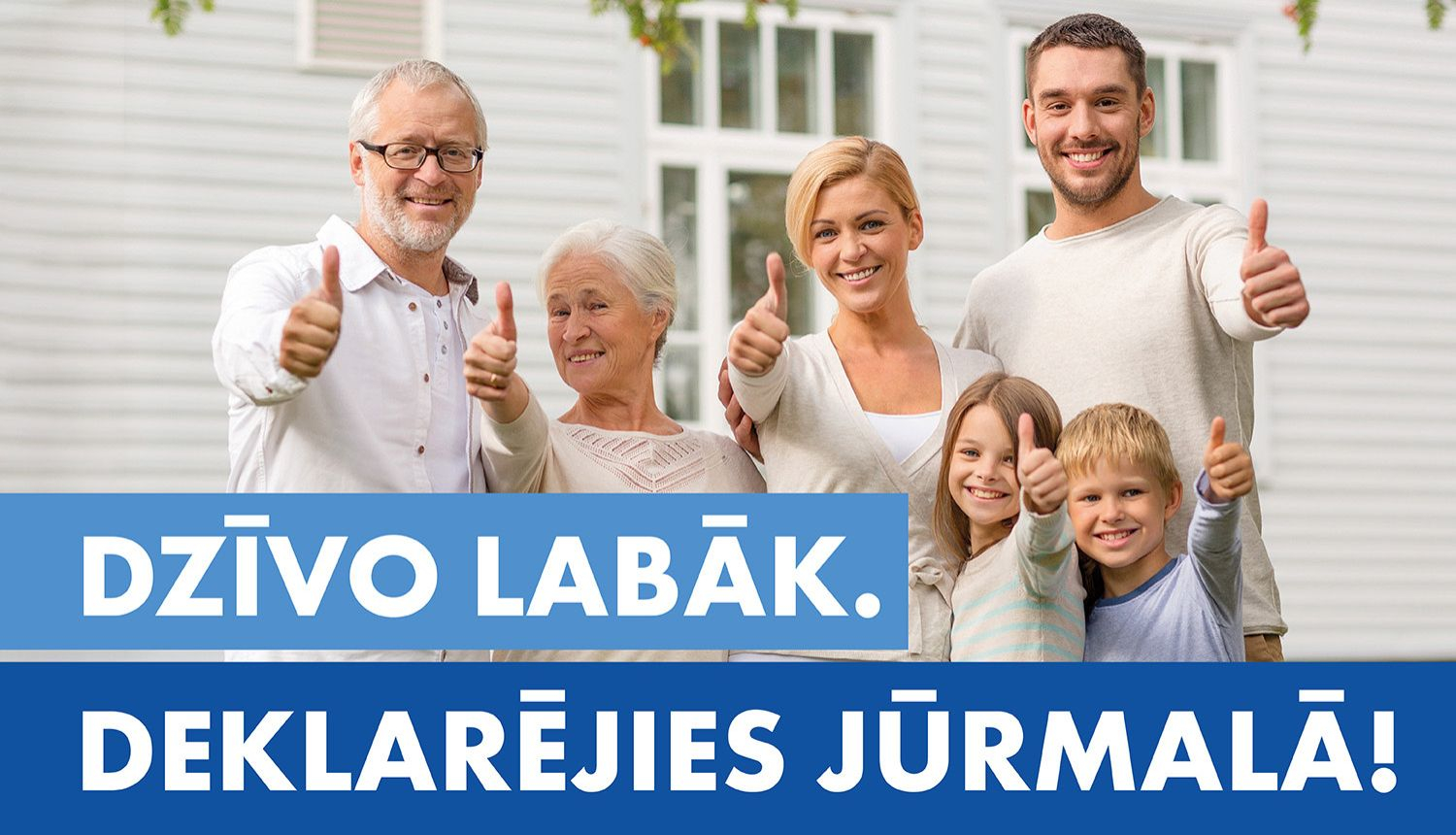 Dažādu paaudžu cilvēku grupa stāv pie gaišas mājas fasādes un smaidot rāda paceltus īkšķus; attēla apakšdaļā redzams teksts ‘Dzīvo labāk. Deklarējies Jūrmalā