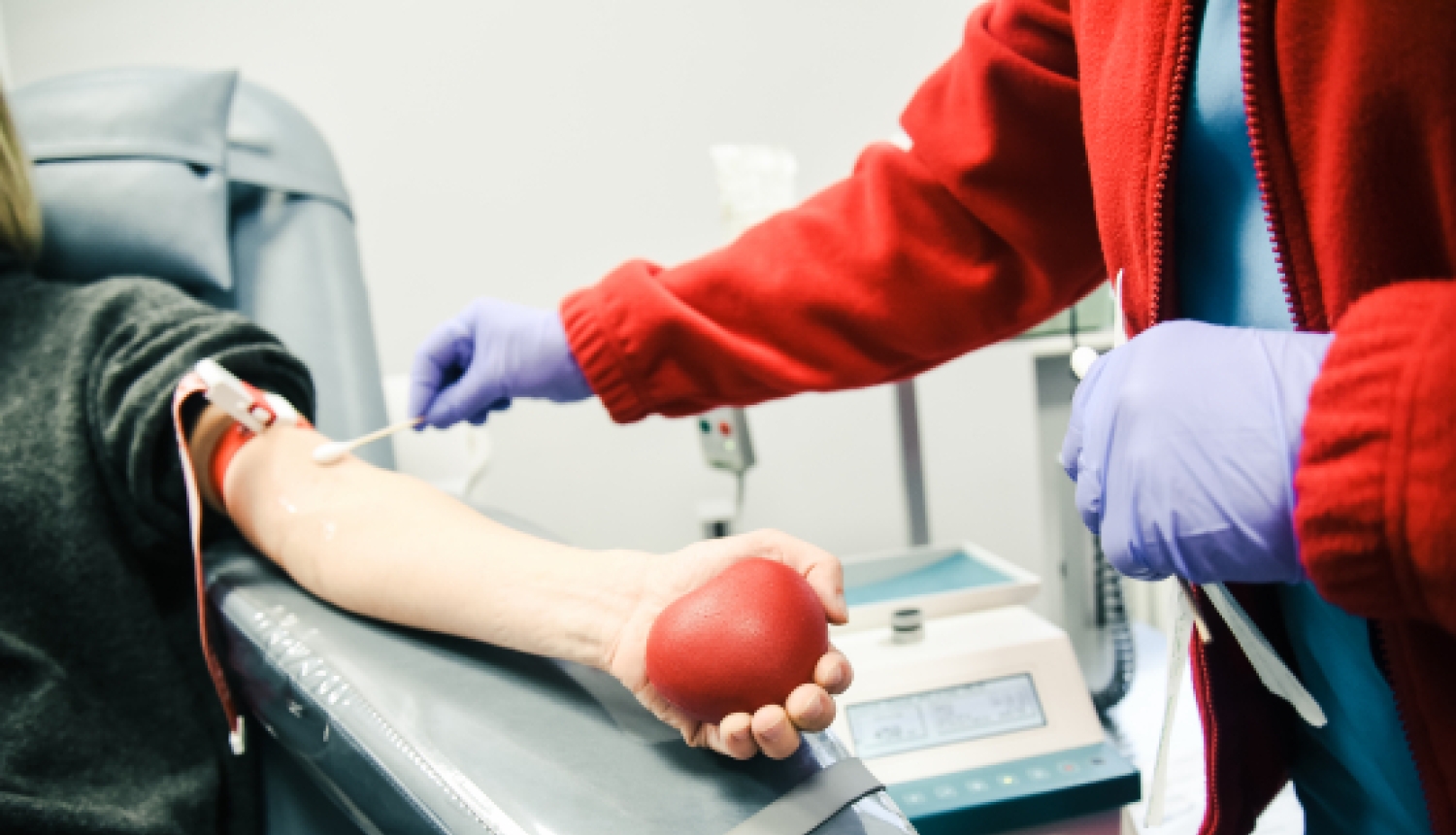 Medicīnas darbinieks ņem asins paraugu no donora, kurš rokā tur sarkanu bumbiņu.
