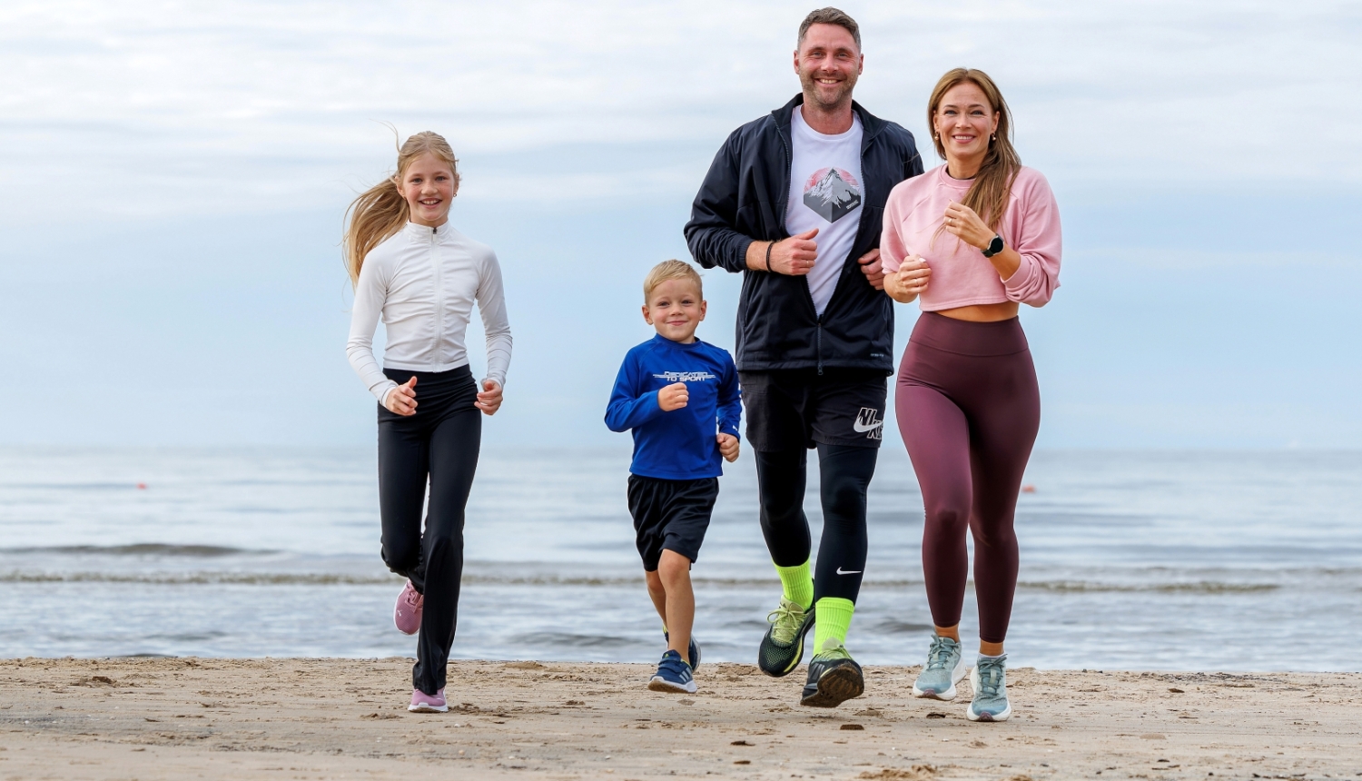 sportiska ģimene skrien gar jūru