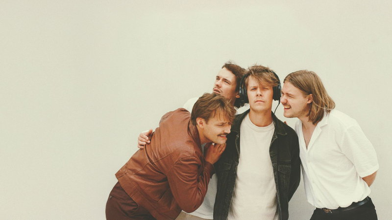 vienas grupas četri puiši stāv pie sienas