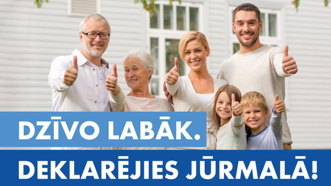 Dažādu paaudžu cilvēku grupa stāv pie gaišas mājas fasādes un smaidot rāda paceltus īkšķus; attēla apakšdaļā redzams teksts ‘Dzīvo labāk. Deklarējies Jūrmalā