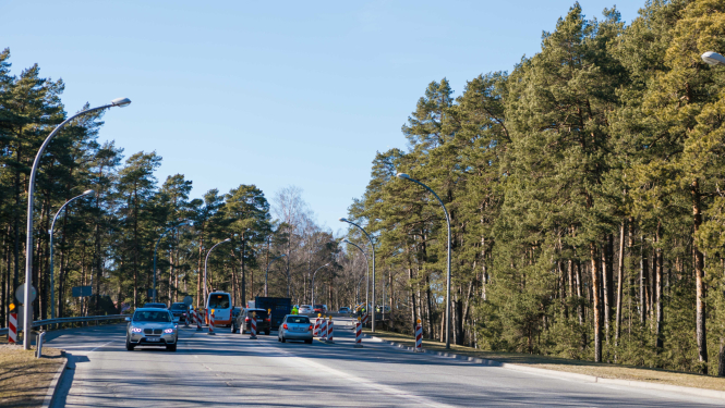 Satiksme uz meža ieskauta ceļa ar ceļa zīmēm un konusiem, kas norāda uz būvdarbiem