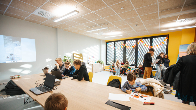 Skolēni dažādos vecumos piedalās radošās un digitālās aktivitātēs modernā, krāsaini noformētā telpā