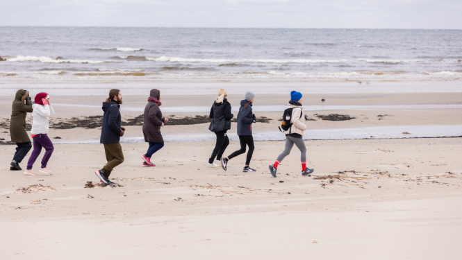 cilvēki skrien gar jūru