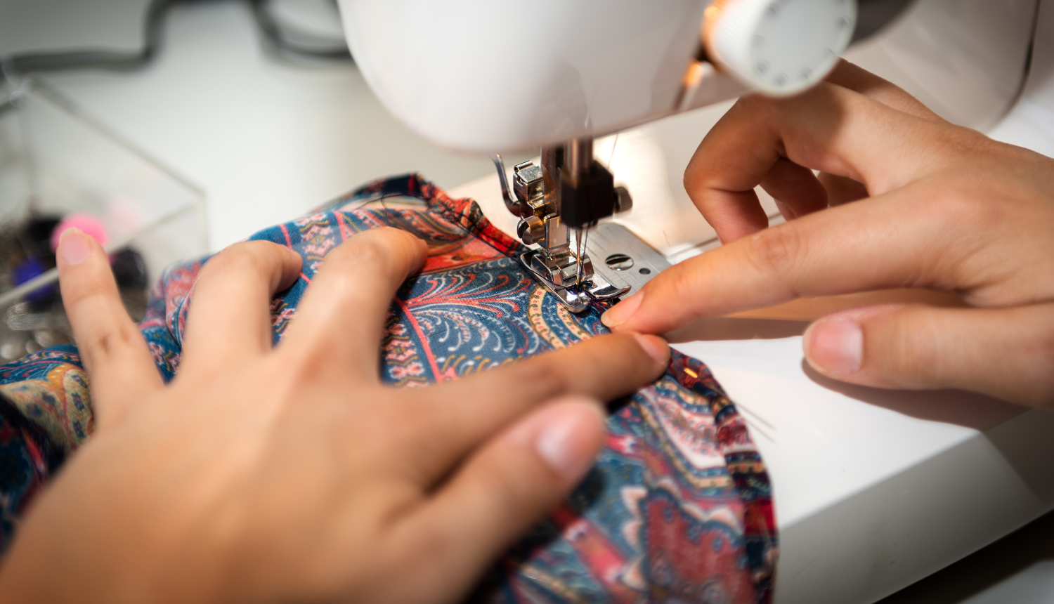 Tuvplāns ar rokām, kas šuj rakstainu audumu ar šujmašīnu.