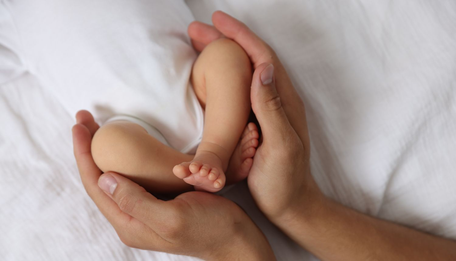 Pieaugušā rokas maigi tur zīdaiņa kājas