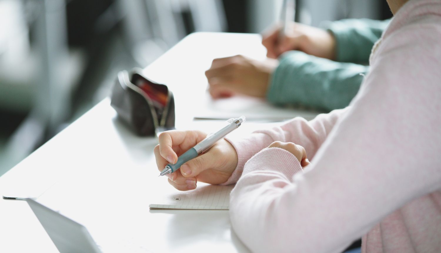 Skolēni sēž pie galdiem un raksta kladēs, piedaloties mācību darbā vai olimpiādē