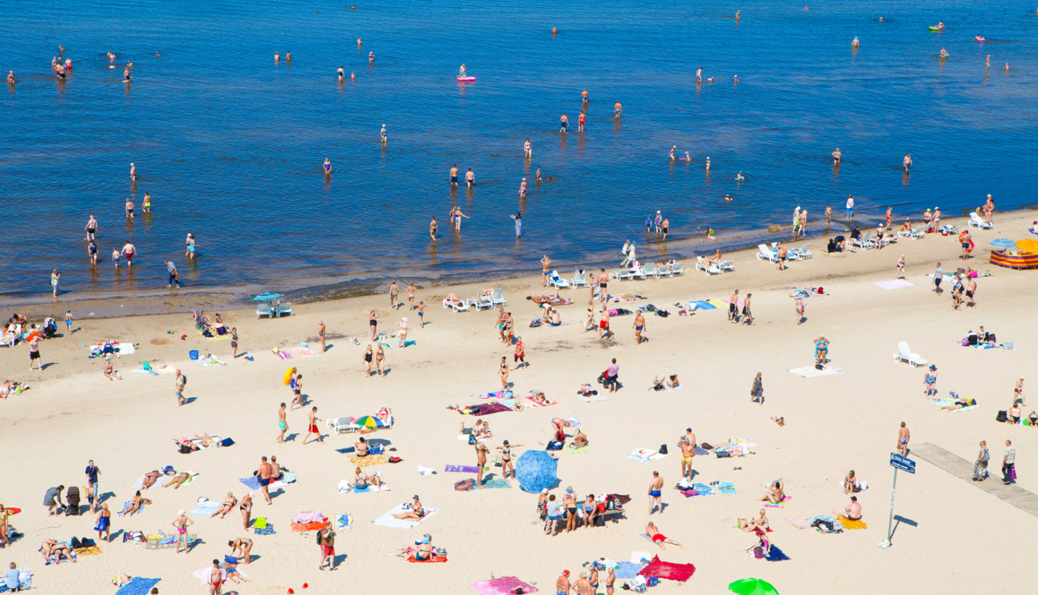 "Vasara pludmalē ar daudz cilvēkiem, kas bauda saulainu dienu