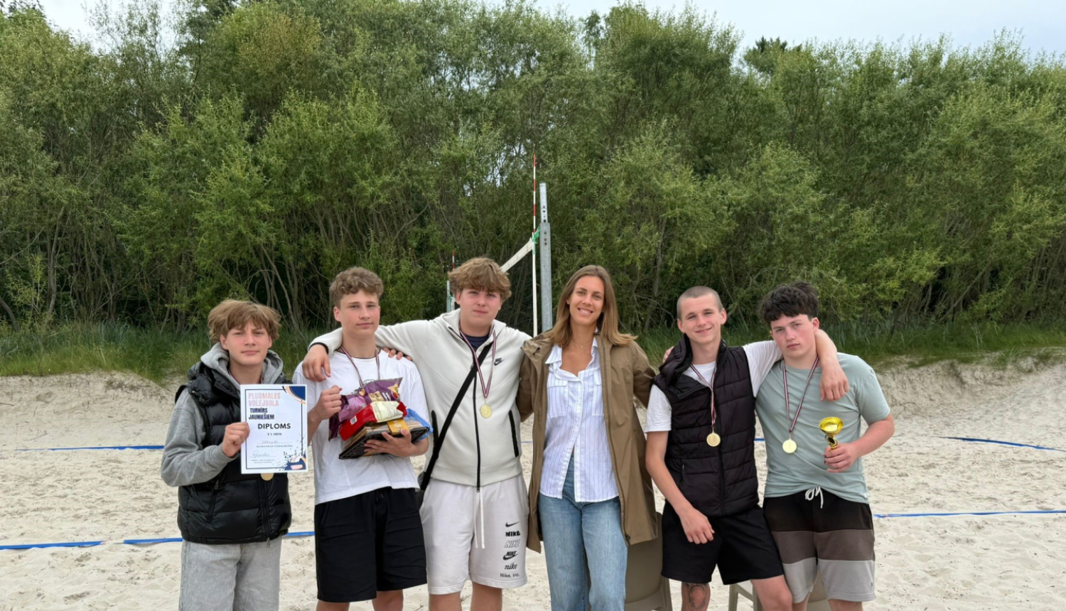 Grupa jauniešu un trenere pludmalē pēc pludmales volejbola turnīra