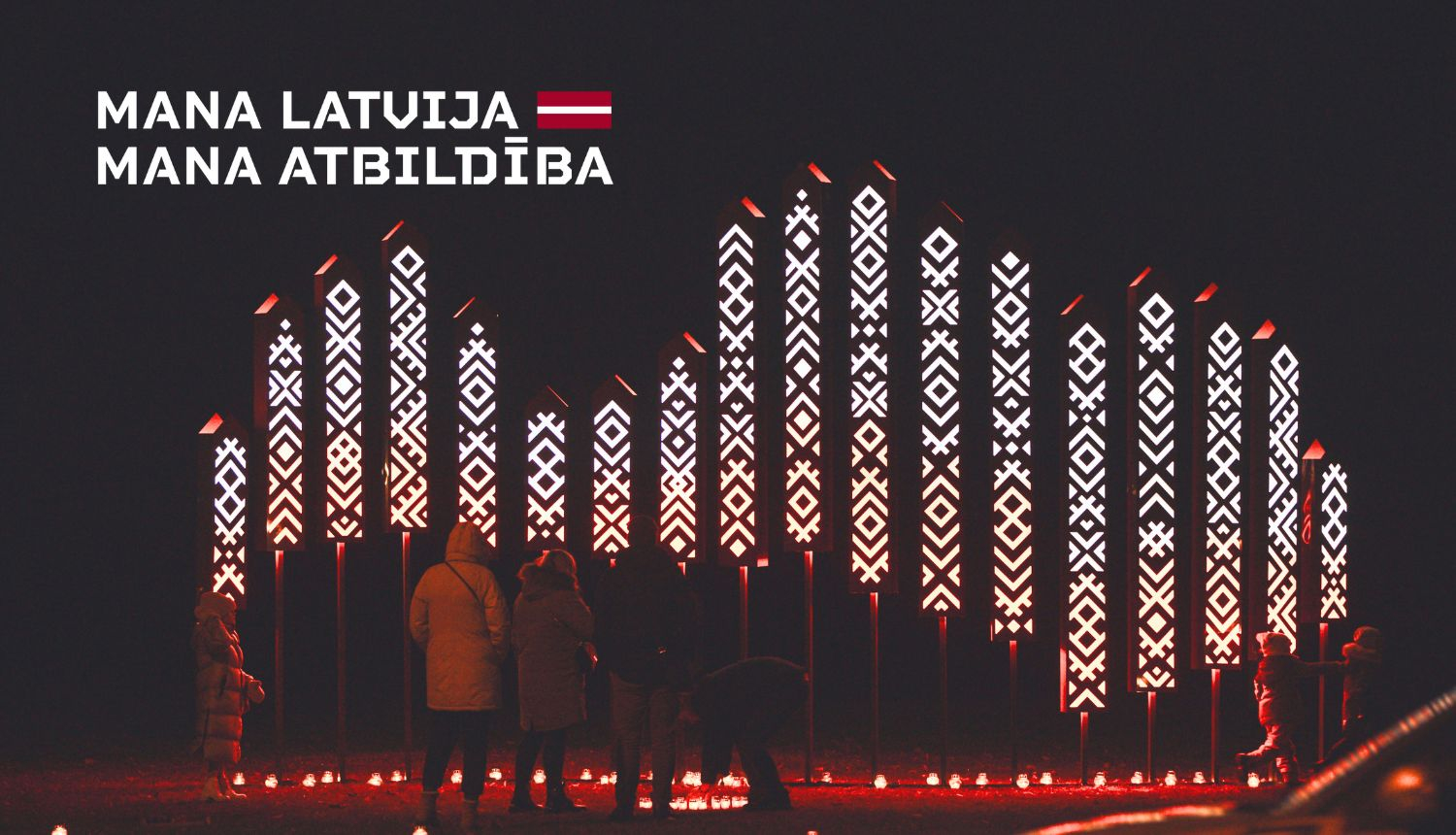 instalācija ar izgaismotiem stabiem, kuros redzami latviešu etnogrāfiskie raksti sarkanbaltos toņos